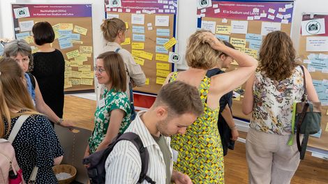 Im Hintergrund stehen Pinw&auml;nde mit den WS-Ergebnissen. Davor sind viele Teilnehmenden in dabei, sie zu bearbeiten oder miteinander zu reden.