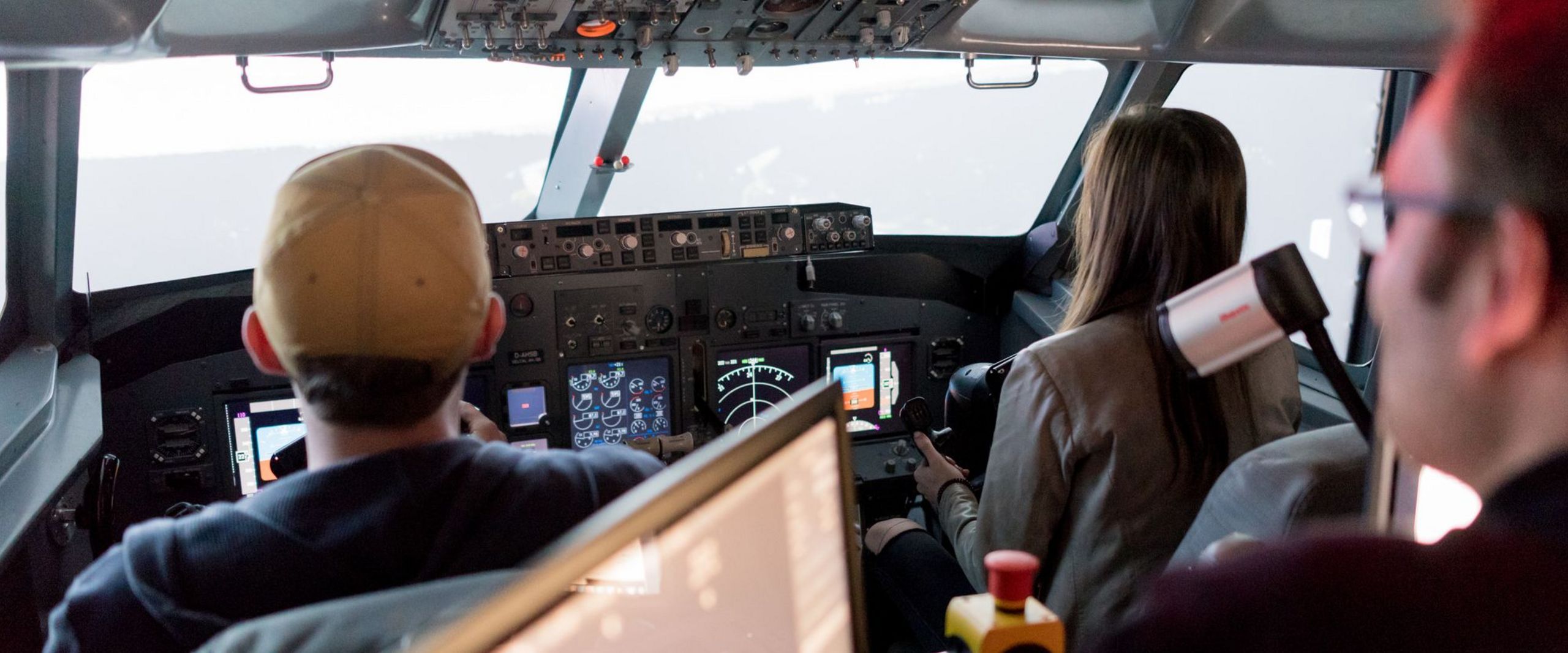 Zwei Studierende und ein Professor sitzen im Cockpit eines Flugsimulators.