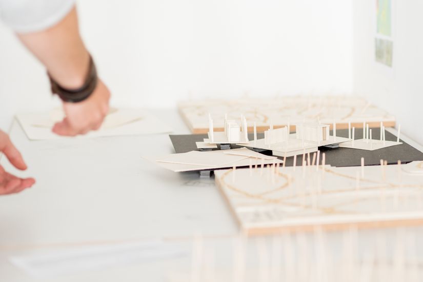 Eine Hand deutet auf architektonische Modelle von Gebäuden.  Eine Hand deutet auf architektonische Modelle von Gebäuden.