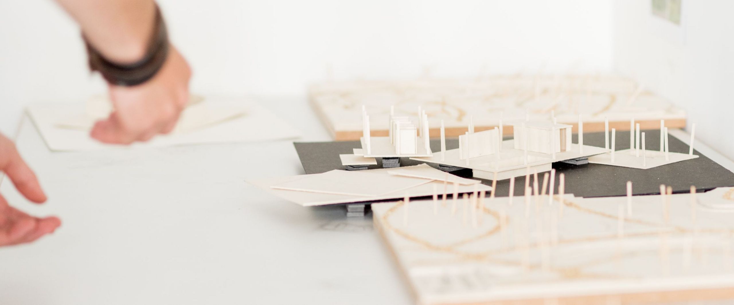 Eine Hand deutet auf architektonische Modelle von Gebäuden.  Eine Hand deutet auf architektonische Modelle von Gebäuden.