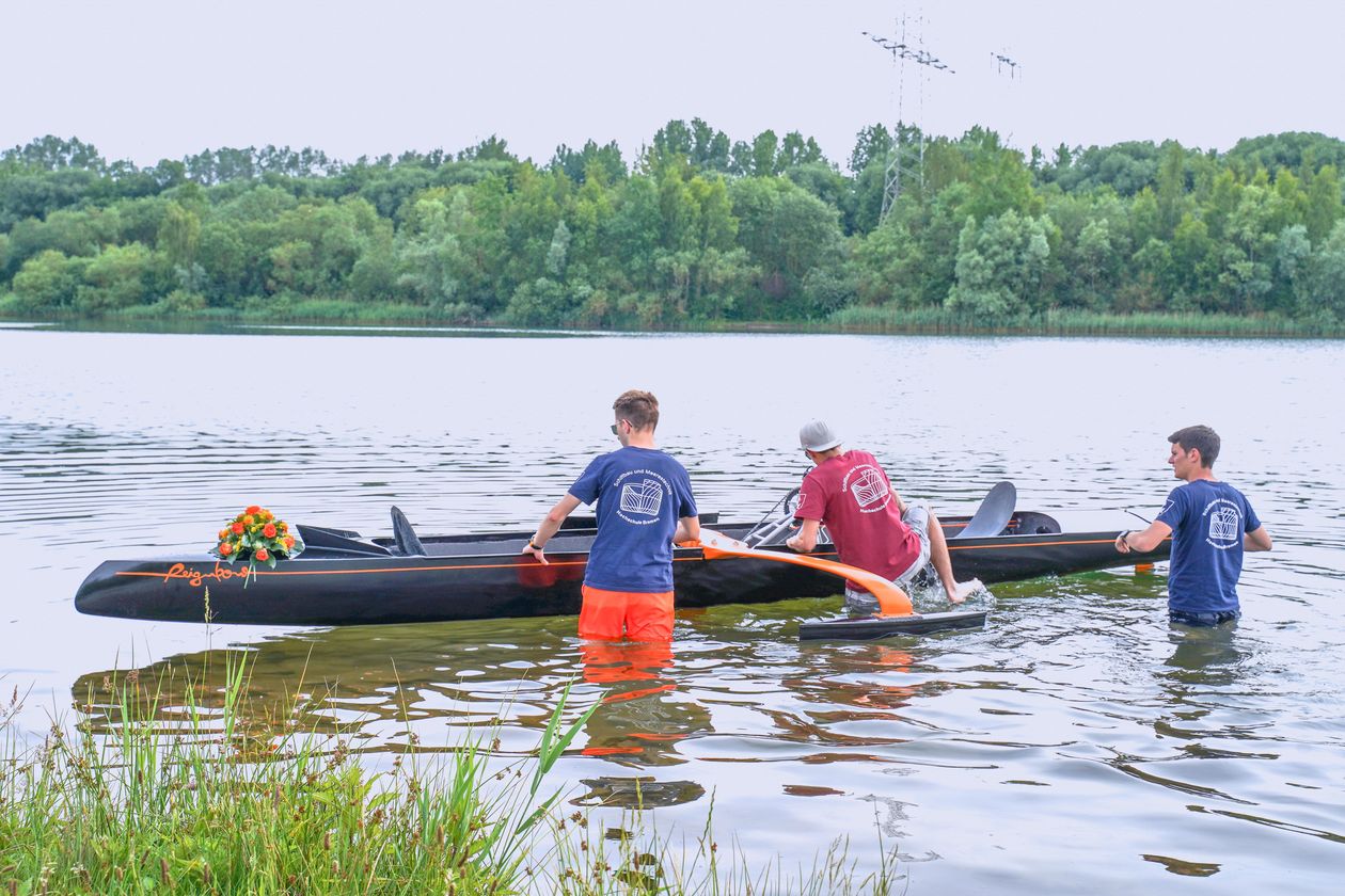 Jungfernfahrt Tretboots Reignbow, das Boot wird von 3 Studierenden zu Wasser gelassen.