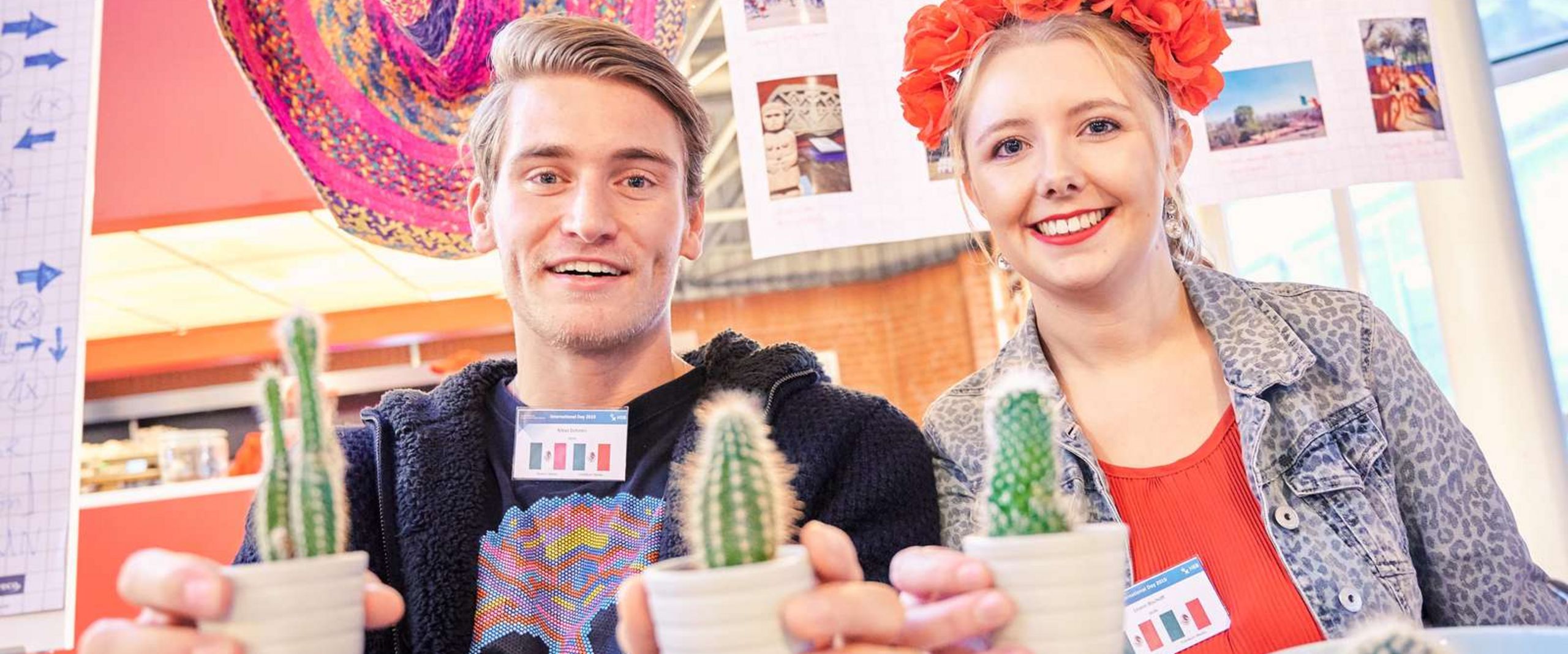 International Day 2025 Zwei Studierende mit Kakteen und buntem Hintergrund zum Thema Mexiko.