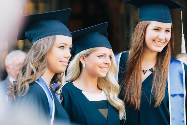 Drei Absolventinnen gekleidet in Roben und Doktorhüten stehen nebeneinander und lächeln.