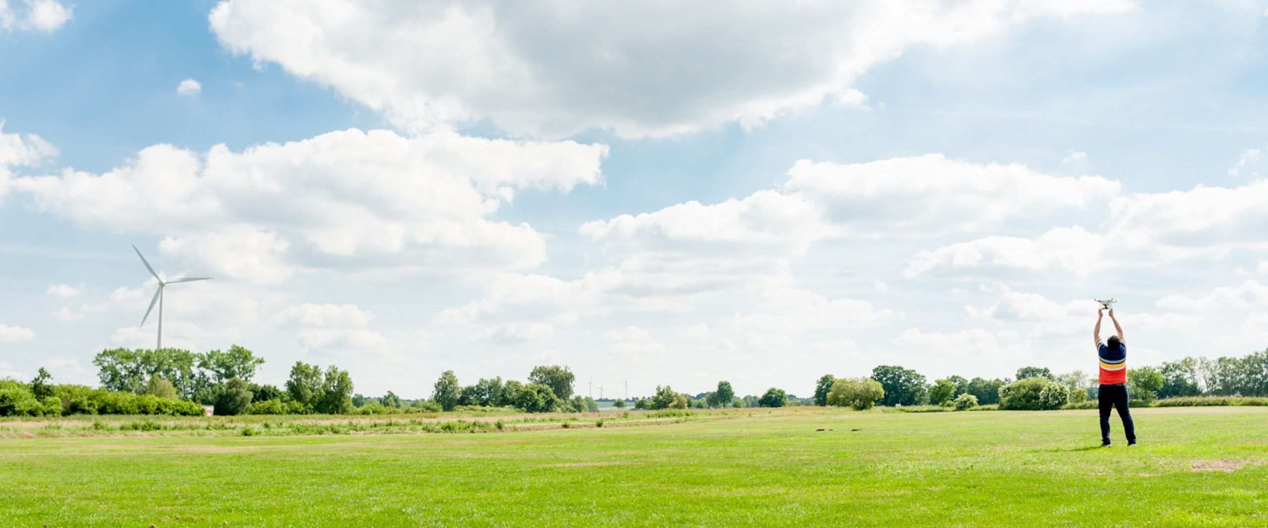 Landschaft Eine grüne Wiese mit blauem Himmel, welcher teilweise bewölkt ist.