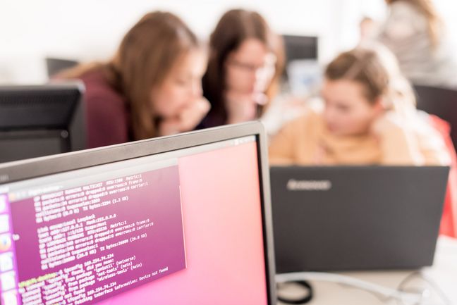 Drei Studentinnen programmieren an einem Laptop. 