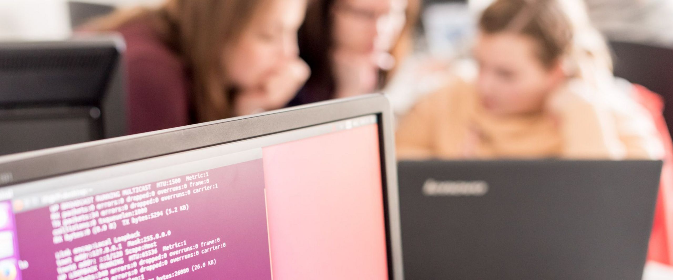 Drei Studentinnen programmieren an einem Laptop. 