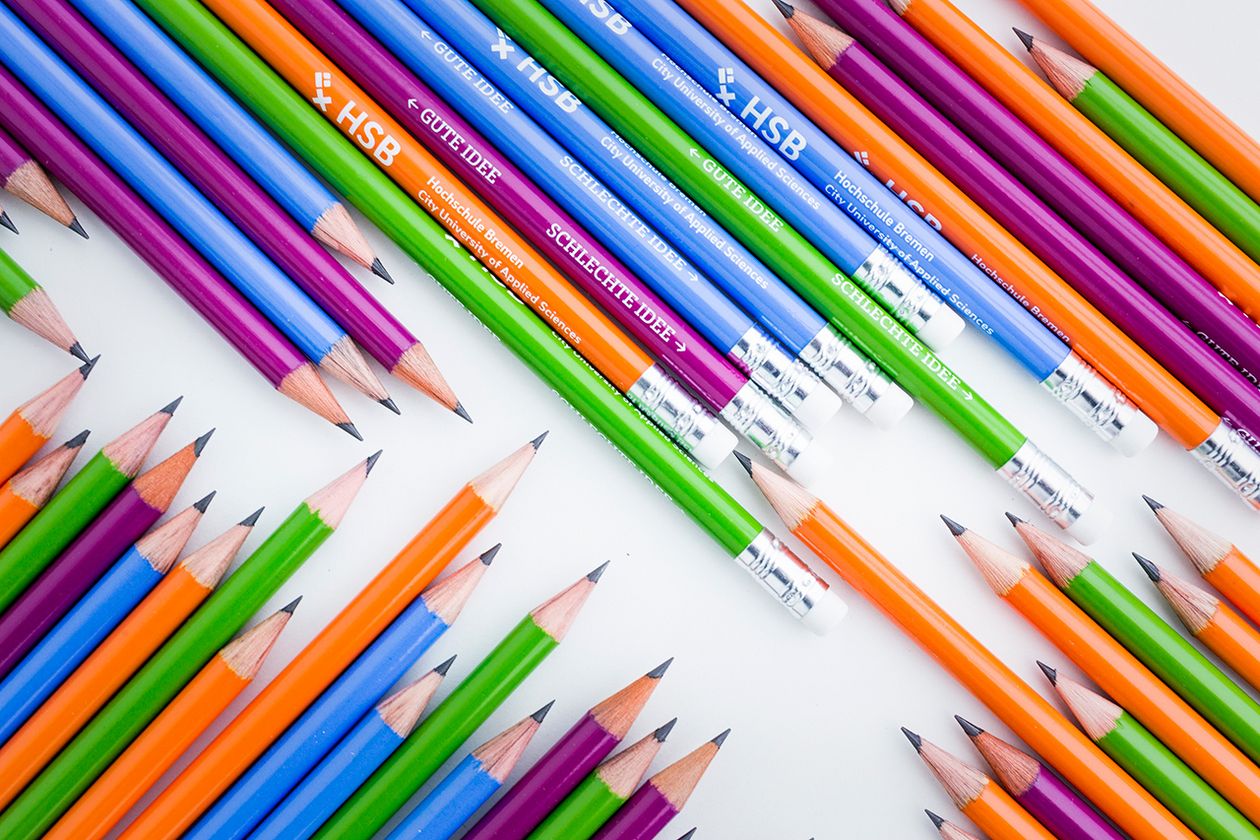 Nebeneinander liegen mehrere blaue, grüne, violette und orangene Bleistifte, die das HSB-Logo tragen.