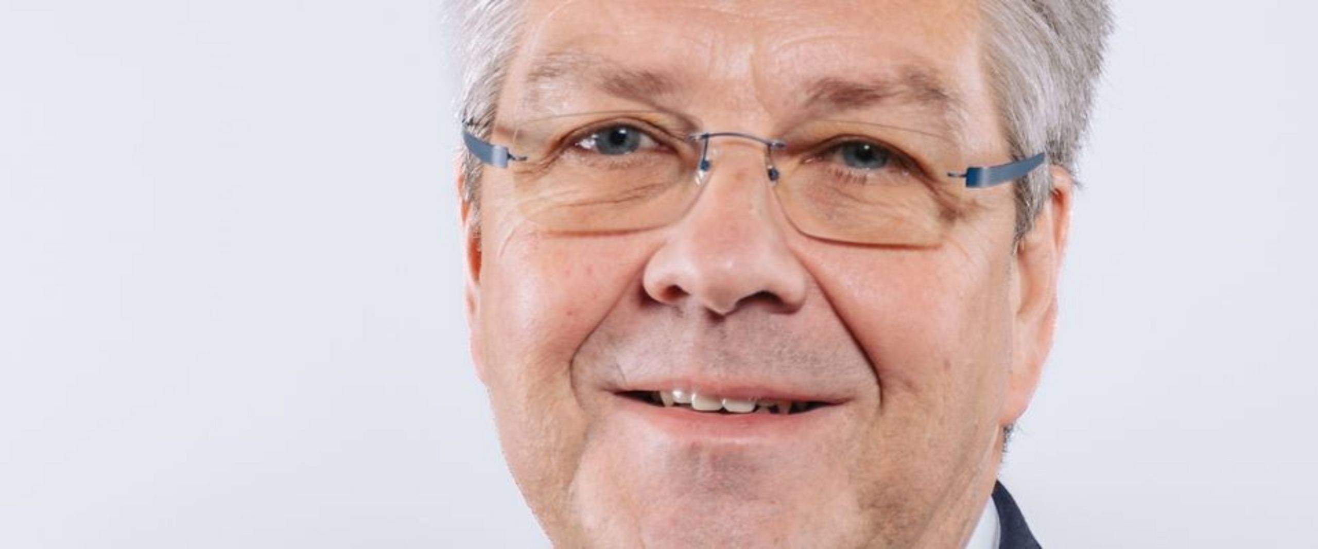 Auf dem Foto ist Helge Ellwart zu sehen. Er hat kurzes graues Haar und trägt ein weißes Hemd unter einer schwarzen Anzugsjacke. 
