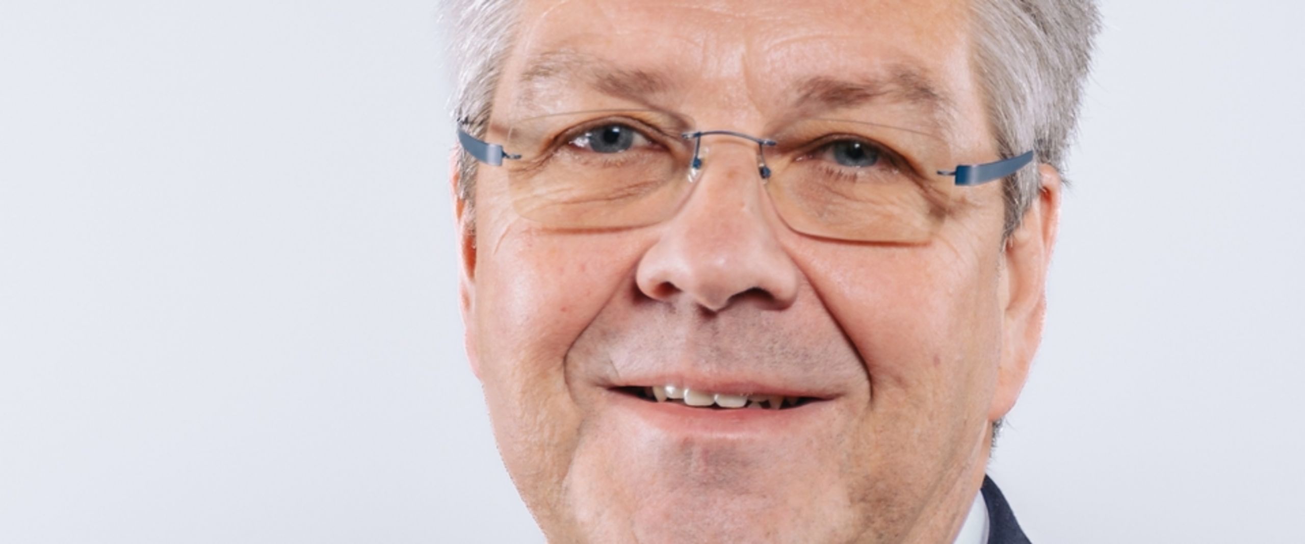 Auf dem Foto ist Helge Ellwart zu sehen. Er hat kurzes graues Haar und trägt ein weißes Hemd unter einer schwarzen Anzugsjacke. 