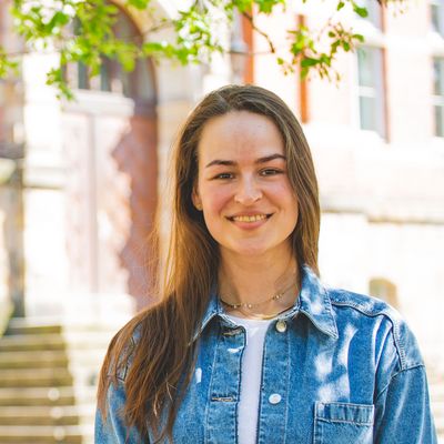 Studentin vor M-Gebäude und grünen Bäumen