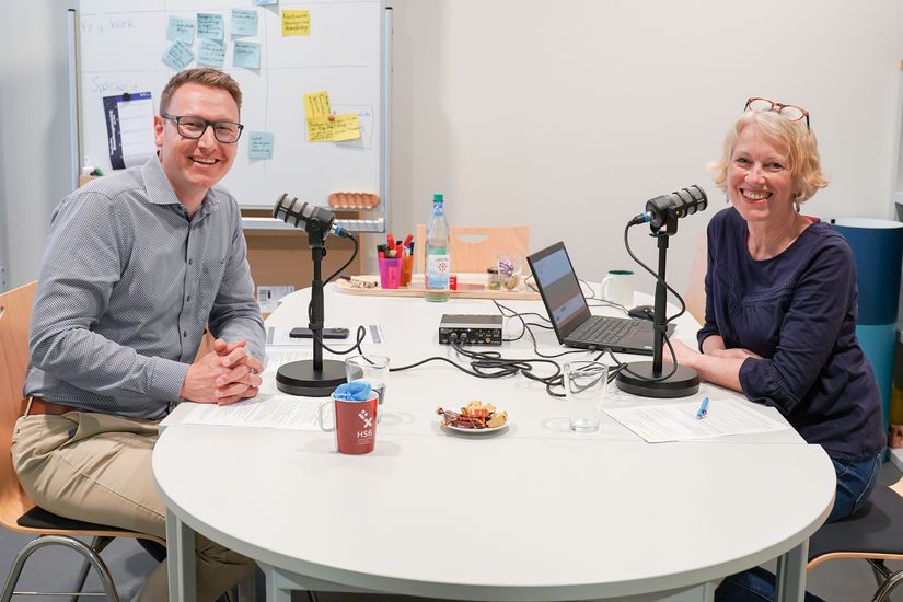 Christian Nolte und Monika Blaschke am Tisch, vor sich große Mikrofone für die Podcastaufnahme