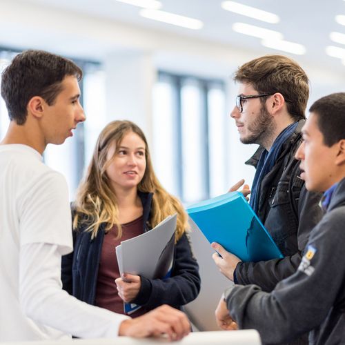 Eine Gruppe Studierender mit Unterlagen in der Hand unterh&auml;lt sich. 