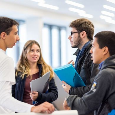 Eine Gruppe Studierender mit Unterlagen in der Hand unterhält sich. 