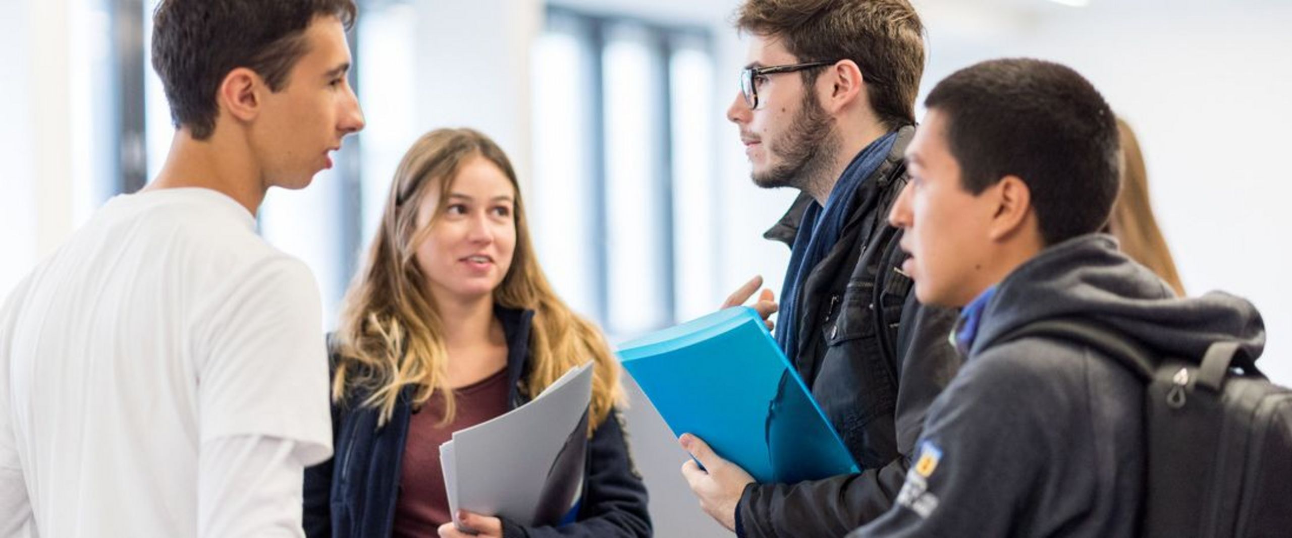 Eine Gruppe Studierender mit Unterlagen in der Hand unterhält sich. 