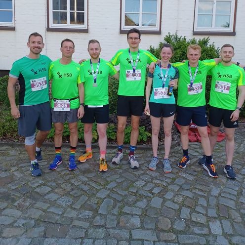 Sieben Sportler der HSB TriRunners posieren nebeneinander in Sportkleidung.