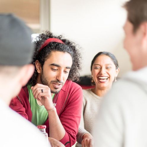 Eine Gruppe von Studierenden sitzt an einem Tisch. Sie lachen und blicken teilweise auf ein Tablet vor ihnen auf dem Tisch.