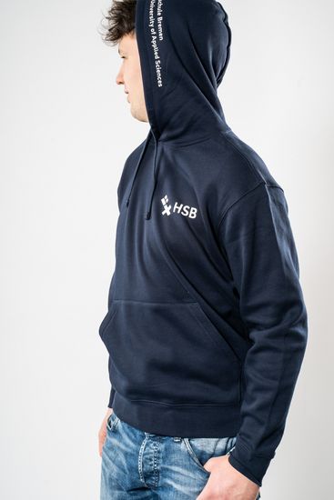 Das Model trägt einen dunkelblauen Pullover für Herren mit dem HSB-Logo darauf und wird dabei von der Seite gezeigt.