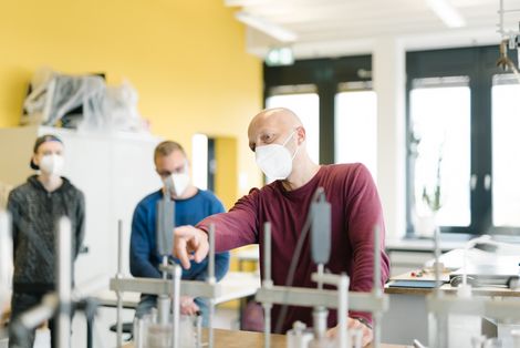 Ein Professor zeigt zwei Studenten etwas an einem Experiment im Geotechniklabor