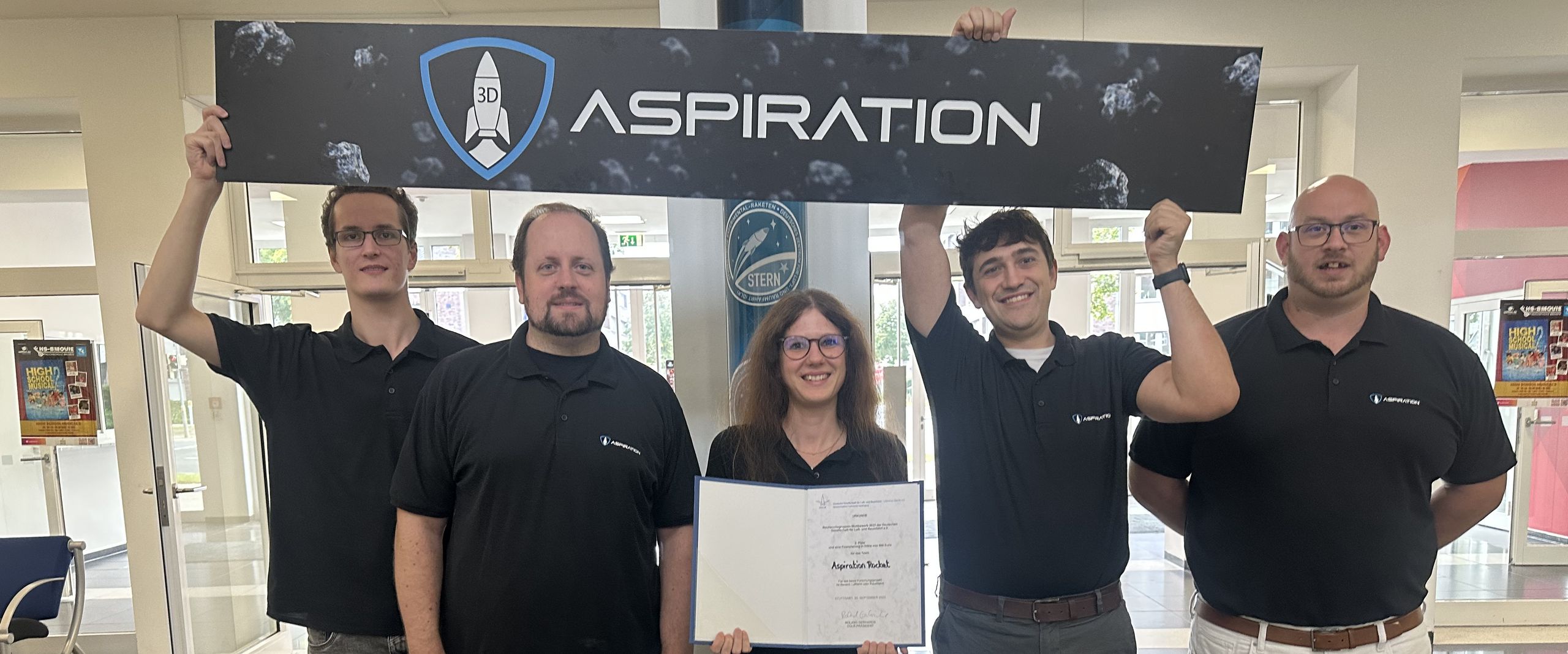 gruppenbild mit vier M&auml;nnern und einer Frau. Sie halten ein Plakat und eine Urkunde.