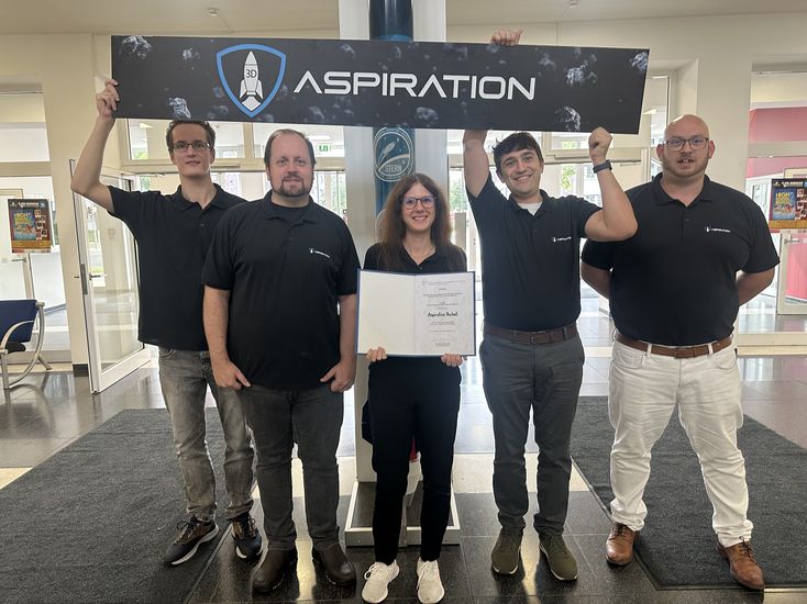 gruppenbild mit vier Männern und einer Frau. Sie halten ein Plakat und eine Urkunde.