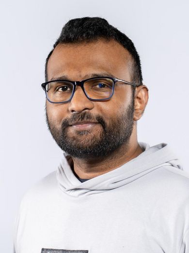 Auf dem Foto ist Abby Kandathil Abraham zusehen. Er hat kurzes schwarzes Haar und einen Bart. Er tr&auml;gt eine Brille und einen wei&szlig;en Kaputzenpullover. 