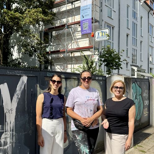 202608 Mural City Scharff rethfeldt und Güttler mit Künstlerin gruppenbild mit drei Frauen vor einer Hausfassade, an der ein Wandbild entsteht