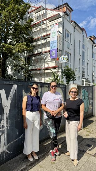 gruppenbild mit drei Frauen vor einer Hausfassade, an der ein Wandbild entsteht