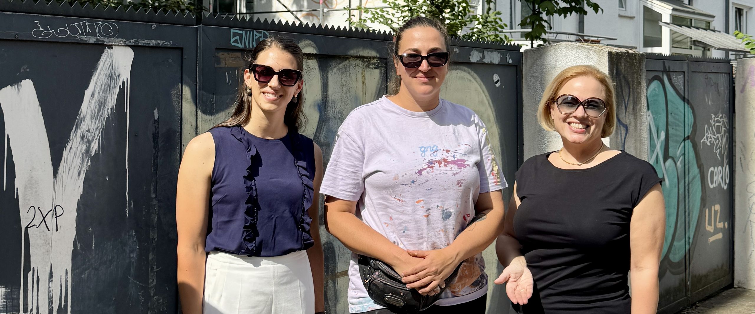 gruppenbild mit drei Frauen vor einer Hausfassade, an der ein Wandbild entsteht