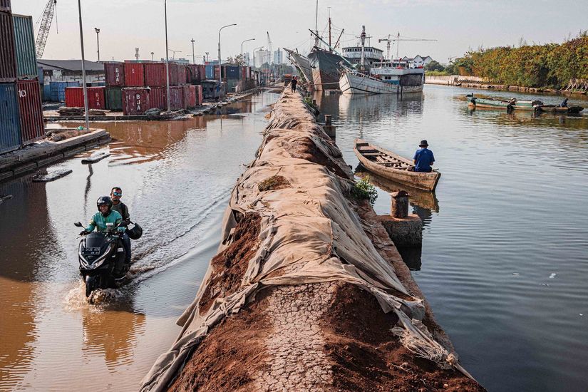 Ein Erddamm trennt Wasser. Links fährt eine Vespa durch das wasser, rechs ein Boot. Auf dem Bild sind zudem Container und Schiffe zu sehen.