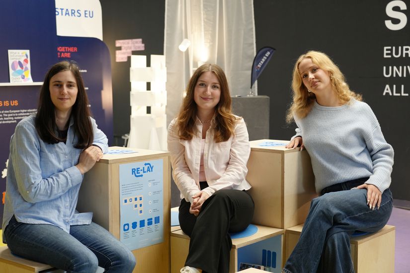 Three young people are sitting on small wooden boxes and smiling at the camera