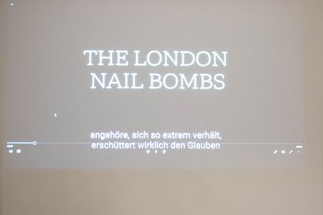 Ein Beamerbild an einer Wand. Es läuft gerade ein Video mit dem Thema "The London Nail Bombs".
