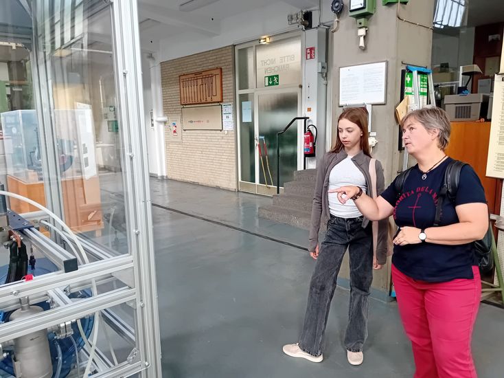 Frau und Mädchen stehen in einer Halle und schauen auf ein großes Forschungsgerät