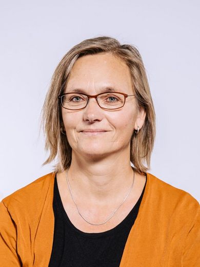 Auf dem Bild ist Regine Kosmoss zu sehen. Sie hat glattes hellbraunes Haar. Sie trägt eine Brille und eine orangene Jacke