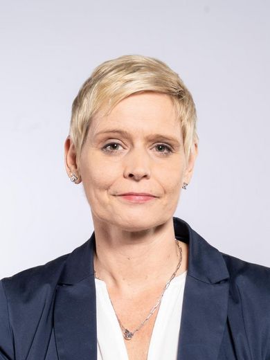 Auf dem Bild ist Bärbel von Grönheim zu sehen. Sie hat kurzes blondes Haar und trägt eine weiße Bluse mit dunkel blauem Blazer. 