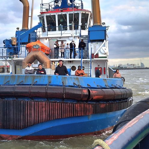 Zwei Schlepperboote begegnen sich im Hafengelände. Am Bug eines der Schiffe stehen HSB-Studierende und winken in die Kamera.