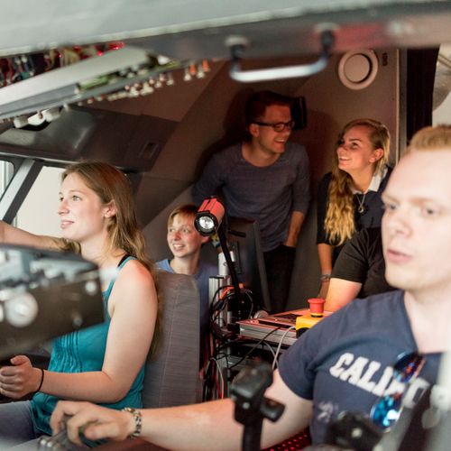 Junge M&auml;nner und Frauen sitzen im Cockpit eines Flugsimulators. 