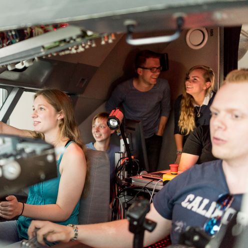 Junge M&auml;nner und Frauen sitzen im Cockpit eines Flugsimulators. 