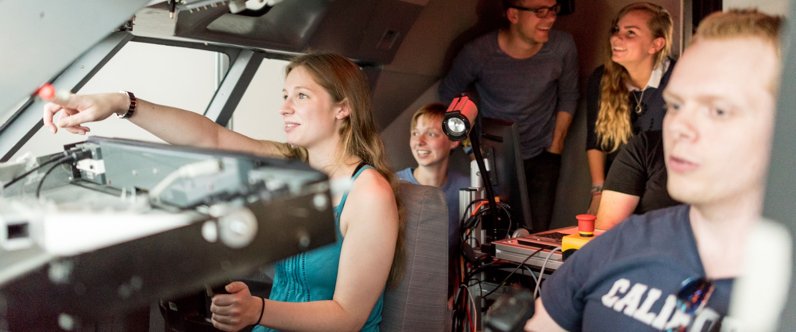 Junge M&auml;nner und Frauen sitzen im Cockpit eines Flugsimulators. 