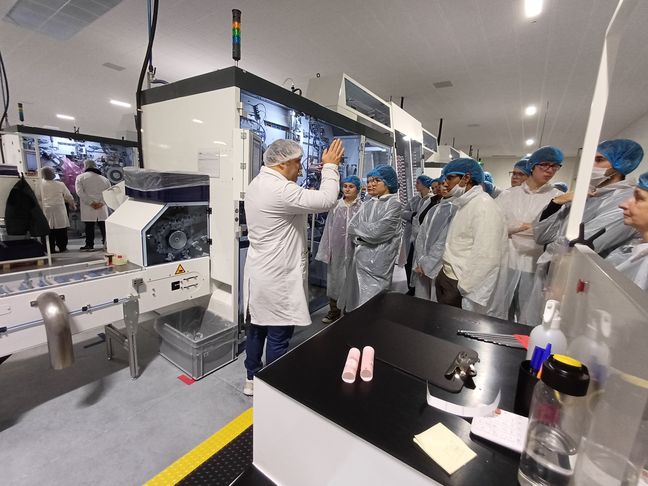 Studierende in Kitteln und Haarnetzen vor einer Verpackungsmaschine 