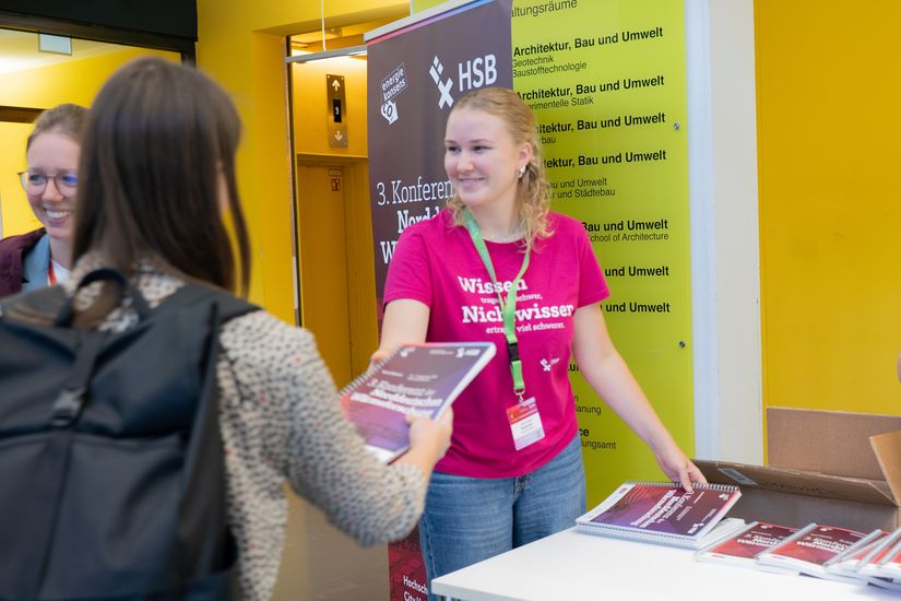 Studentin händigt books of Abstracts an Besucher:innen der 3. Konferenz der Norddeutschen Wärmeforschung aus.