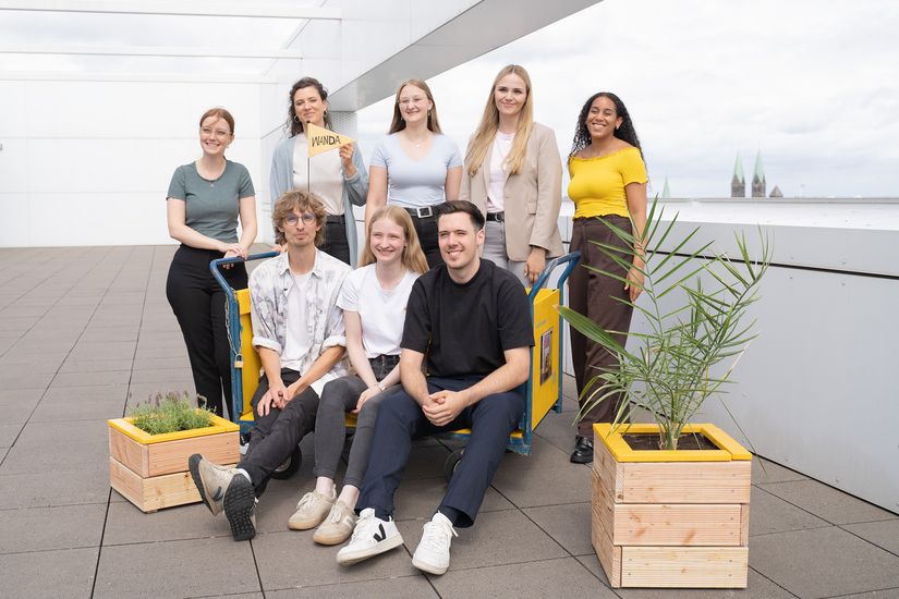 gruppenbild mit jungen M&auml;nnern und Frauen Neben ihnen stehen kleine Pflanzenk&uuml;bel aus Holz