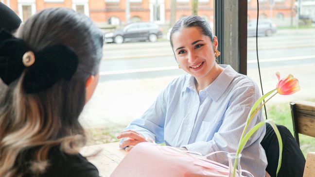 Junge Frau im Gespräch mit Studentin an einem Tisch