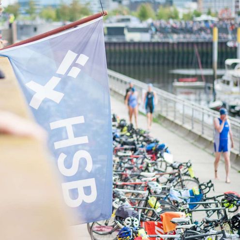 Eine blaue Fahne mit dem HSB Logo wird von einem Mann gehalten. Im Hintergrund ist der Marina Hafen in Bremen-&Uuml;berseestadt zu sehen.