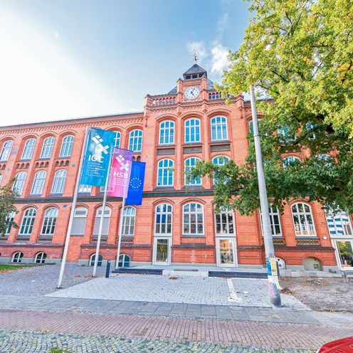 IGC_HSB_mit Flaggen Panorama-Foto des IGC Gebäudes. Vor dem Gebäude sind Flaggen mit den Logos der HSB und des IGC und eine Europafahne an Masten aufgehängt.