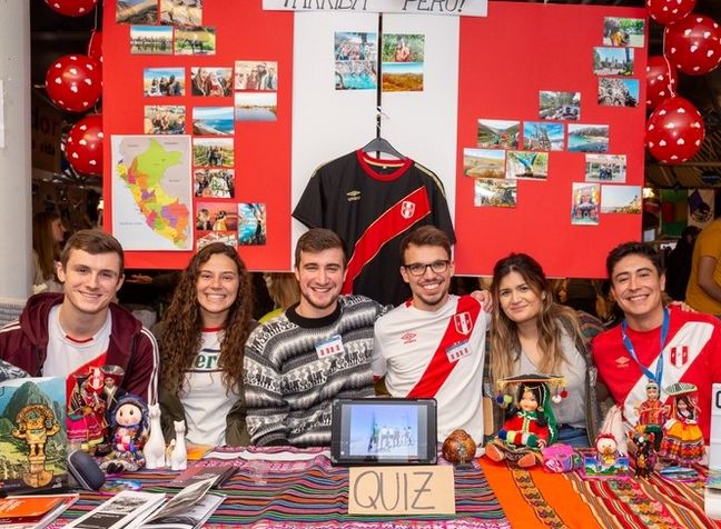 6 Studierende sitzen vor einem selbstgestaltetem Ländertisch und präsentieren damit ihr Auslandssemester in Peru