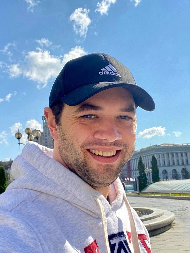 Christian Paluschkewitz Auf dem Foto ist Christian Paluschkewitz zusehen. Seine Haare sind unter einer dunkelblauen Cap versteckt. Er hat einen leichten braunen Bart un trägt einen grauen Kaputzenpullover.