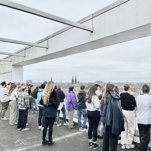 gruppe von Menschen steht auf einer Dachterrasse und schaut in die Ferne