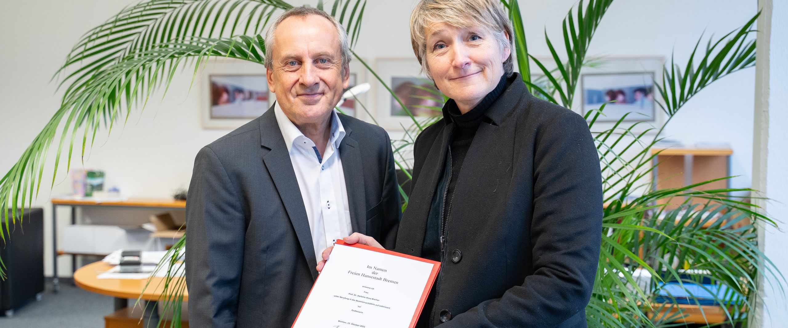Rektor Prof. Dr. Konrad Wolf und Prof. Dr. Stefanie Bremer. schauen in die Kamera. Frau Bremer h&auml;lt ihrer Ernennungsurkunde 