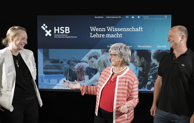 Louisa Karbautzki, Prof. Dr. Karin Luckey und Ole Vorsprecher stehen vor einer Projektion der HSB-Website und freuen sich.