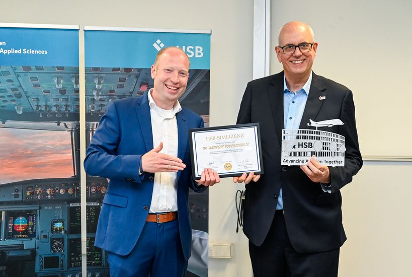 Zwei M&auml;nner halten eine Urkunde und ein Objekt und schauen in die Kamera.